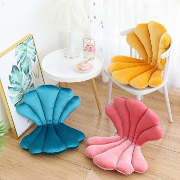 Shell-shaped cushions in blue, pink, and yellow on a wooden floor with a white chair and table in the background.