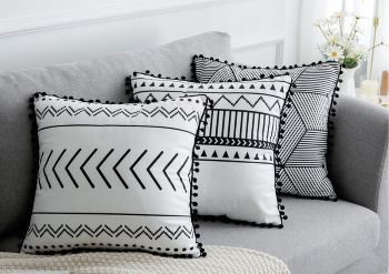 Three decorative throw pillows with black geometric and tribal patterns on white fabric, styled on a gray sofa.
